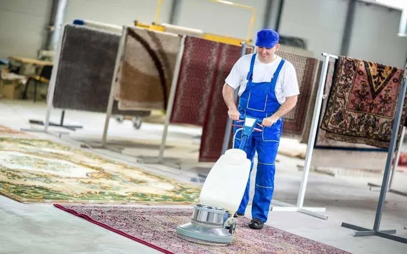 Golvmaskin på en matta i en ljus lokal där tvättade mattor hänger på ställningar